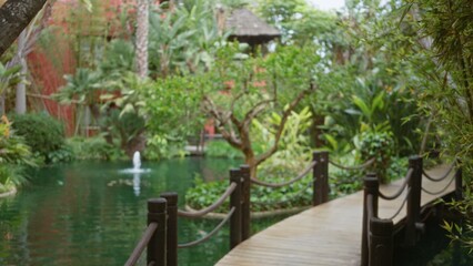 Defocused tropical resort scene with lush greenery framing a tranquil pond and elegant bridge,...