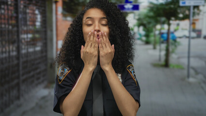 Hispanic policewoman blowing kiss outdoors in uniform on city street with vibrant urban background...