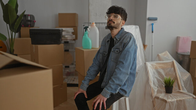 Young man resting in a cluttered living room filled with moving boxes and furniture, showcasing the process of moving into a new home.