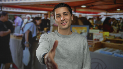 Young man extending hand at a bustling outdoor market with vibrant stalls and diverse shoppers...