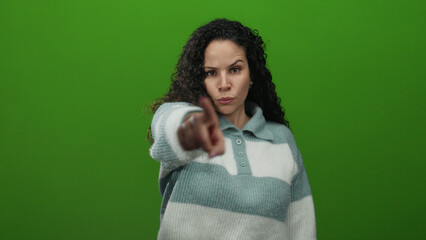 Woman making inviting gesture against green background, wearing striped sweater, expressing...