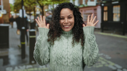 Woman outdoors smiling with curly hair and green sweater on city street with blurred background...