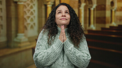 Woman praying in a church setting wearing a cozy sweater, her expression reflecting solemn devotion...