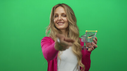 Woman pointing holding small cart against green background isolated wall highlighting supermarket concept.