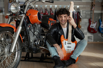 A man holding a guitar stands beside a motorcycle in a vibrant music store setting