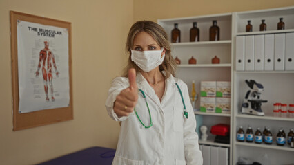 Woman doctor with stethoscope adjusts mask in a clinical office with medical equipment and...