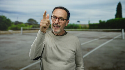 Hispanic man in glasses gestures thoughtfully on an outdoor tennis court, conveying concentration...