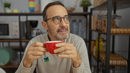 Man relaxing with coffee in cozy indoor office environment displaying thoughtful expression surrounded by casual office decor and shelving units for storage.