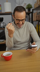 Hispanic middle-aged man in an office celebrating while looking at a smartphone, expressing joy...