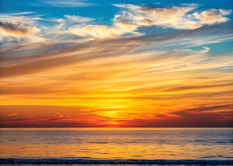 Obraz premium Breathtaking golden orange sunset over calm sea with radiant cloud streaks and vibrant horizon glow 