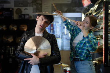 A man holds a cymbal while a woman holds drumsticks