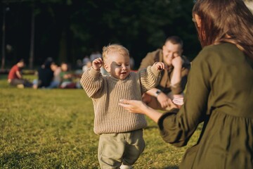 young parents with baby son learning to walk in the park
