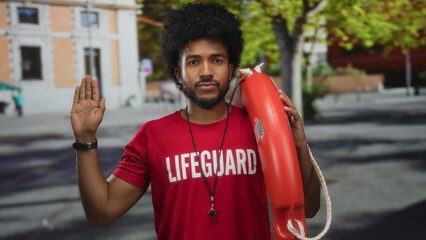 Lifeguard man with an afro hairstyle stands on a city street holding a lifebuoy making an oath...