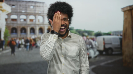Smiling man covers eye in front of the roman coliseum, showcasing vibrant street scene with...