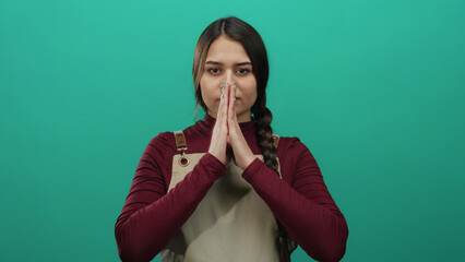 Young woman praying with closed eyes wearing apron against isolated green background suggests peaceful waitress or worker moment of reflection and spirituality.