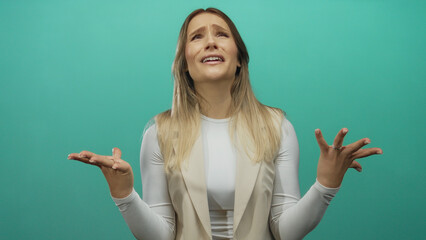 Young woman with blonde hair expressing frustration against a green background wall, conveying...