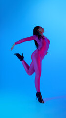 Dancer in vibrant jumpsuit posing elegantly against blue background. Concept of expressive arms and...