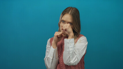 Young woman boxing against isolated blue background with focused expression, showcasing power and determination.