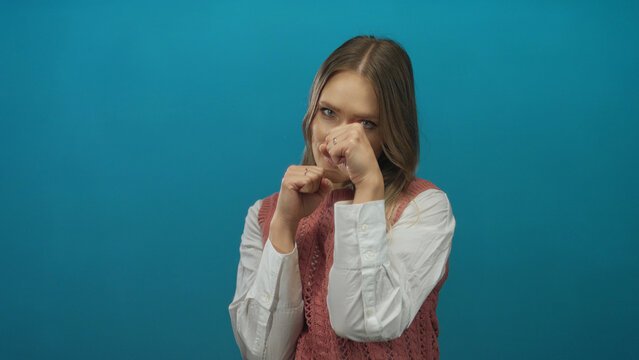 Young woman boxing against isolated blue background with focused expression, showcasing power and determination.