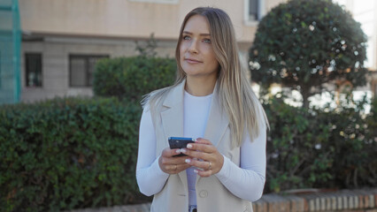 Woman using smartphone in a sunny park showcasing casual outdoor lifestyle, surrounded by greenery...
