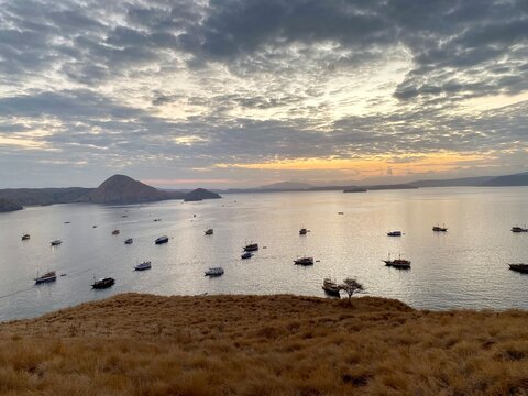 Traditional Phinisi sailing ships sail around the mid-ocean hills of Kelor Island in Komodo National Park, Flores, Indonesia at sunset.