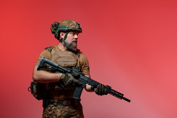 A soldier in military uniform holds a rifle AR 15 in his hands on red background in studio