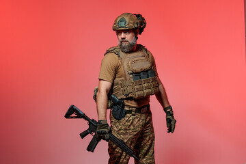 A soldier in military uniform holds a rifle AR 15 in his hands on red background in studio