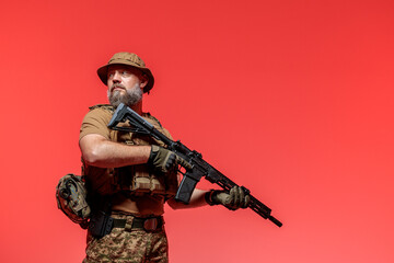A soldier in military uniform holds a rifle AR 15 in his hands on red background in studio