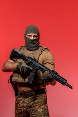 A soldier in military uniform holds a rifle AR 15 in his hands on red background in studio