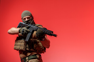 A soldier in military uniform holds a rifle AR 15 in his hands on red background in studio