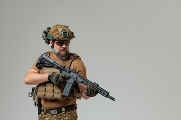 A soldier in military uniform holds a rifle AR 15 in his hands on grey background in studio