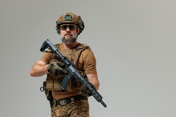 A soldier in military uniform holds a rifle AR 15 in his hands on grey background in studio