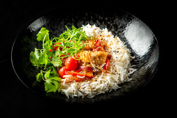 Bowl of cooked white rice topped with fresh vegetables, sesame seeds, and cilantro on dark...