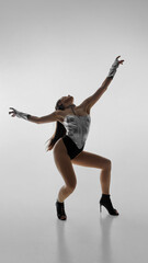 Dancer in silver leotard striking dynamic pose in high heels against white background. Concept of...