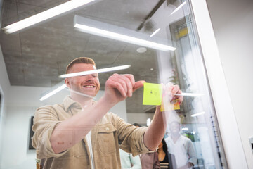 Creative manager attaching colorful sticky notes on a glass wall, sharing ideas and strategies...