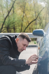 A Caucasian man inspects damage to his car. 