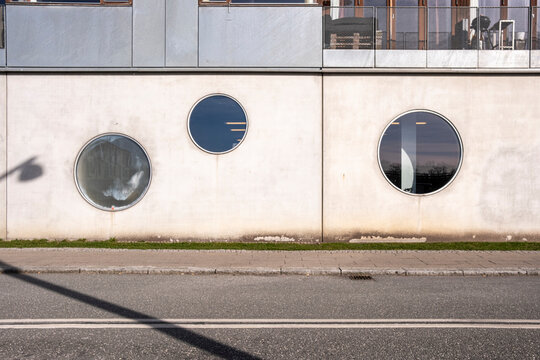 Concrete wall with round windows and shadows on street, combining minimalism, texture and playful geometry in a versatile urban backdrop with strong design language