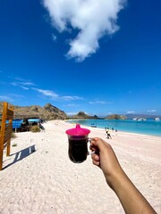 Hand holding Flores black coffee with beautiful pink beach view.