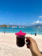 Hand holding Flores black coffee with beautiful pink beach view.