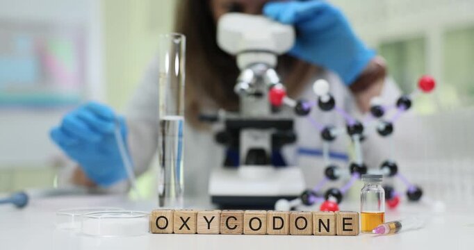 Oxycodone word formed by cubes stands beside microscope and molecule. Female technician explores chemical bond structure measuring substance form
