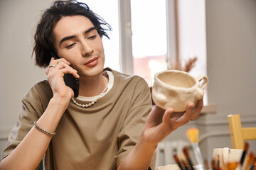 Handsome man engaged in creative pottery work while on the phone in a vibrant studio
