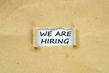 WE ARE HIRING in the middle of torn brown paper. white background.