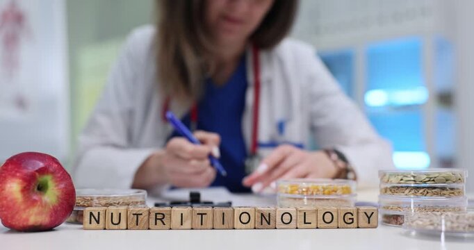 Wooden cubes spell Nutritionology resting near apple and grains. Term reflects balanced living forming connection with food and health science