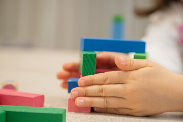 A young child plays indoors during the day, focusing intently while building a structure with colorful wooden blocks, developing fine motor skills, creativity, and early cognitive abilities.