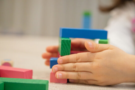 A young child plays indoors during the day, focusing intently while building a structure with colorful wooden blocks, developing fine motor skills, creativity, and early cognitive abilities.