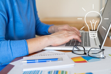 Businesswoman is typing on a laptop with a light bulb icon hovering above, symbolizing the search for innovative solutions in business analysis, finance, and project management