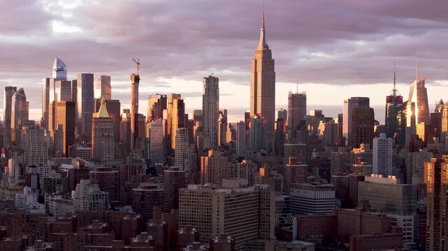 Aerial view of the Empire State Building and other skyscrapers basking in the warm glow of the setting sun, creating a stunning contrast of light and shadow, New York, New York, United States.