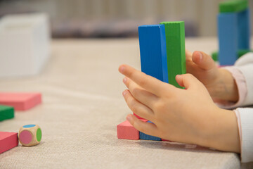 A young child plays indoors during the day, focusing intently while building a structure with colorful wooden blocks, developing fine motor skills, creativity, and early cognitive abilities.