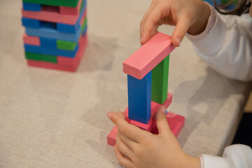 A young child plays indoors during the day, focusing intently while building a structure with colorful wooden blocks, developing fine motor skills, creativity, and early cognitive abilities.