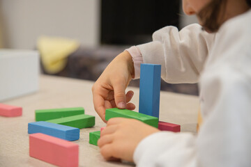 A young child plays indoors during the day, focusing intently while building a structure with colorful wooden blocks, developing fine motor skills, creativity, and early cognitive abilities.